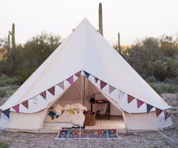 Tienda glamping decorada con banderines, cama doble y alfombra, ideal para estancias en la naturaleza