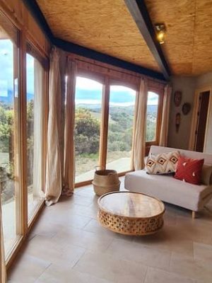 Sofá y mesa artesanal junto a ventanales con vistas a la montaña desde Casa Lucía, en Luz de Sirius